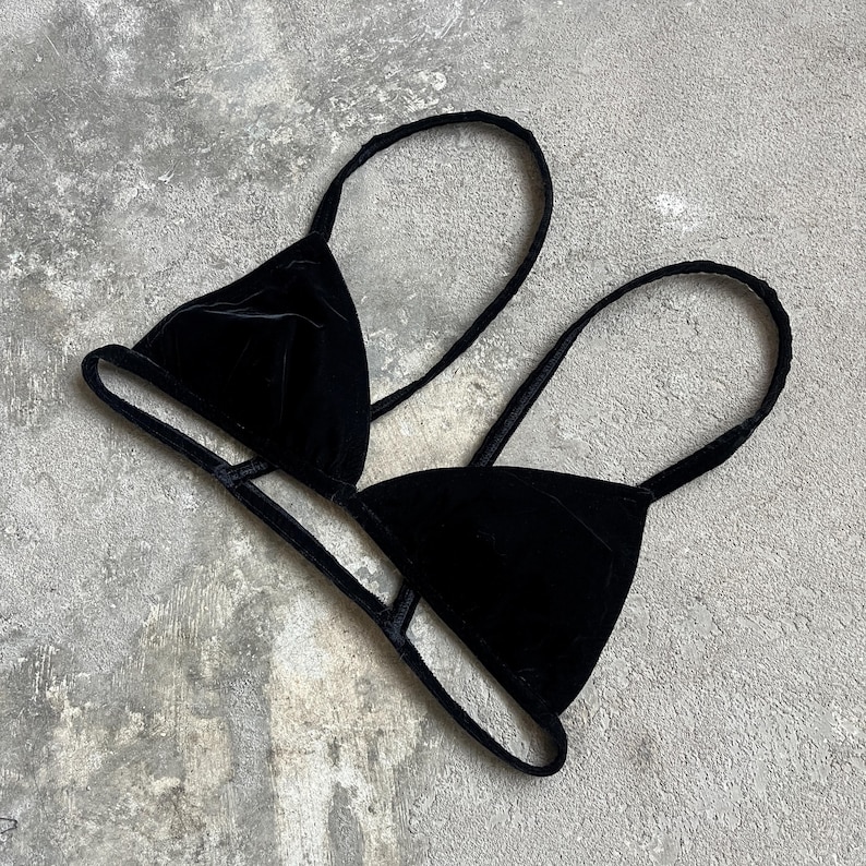 May include: A black velvet triangle bikini top with thin straps. The top is made of a soft, luxurious velvet material and features a classic triangle shape. The straps are thin and adjustable, providing a comfortable fit. The bikini top is designed for swimwear or lingerie.
