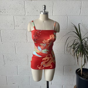 Könnte beinhalten: Ein roter Badeanzug mit Blumen- und Drachenmuster. Der Badeanzug hat dünne Träger und einen quadratischen Ausschnitt.