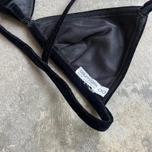 May include: Black velvet triangle bra with thin straps. The bra features a soft, textured fabric and a label that reads "courreges paris made in france". The bra is designed with a classic triangle shape.