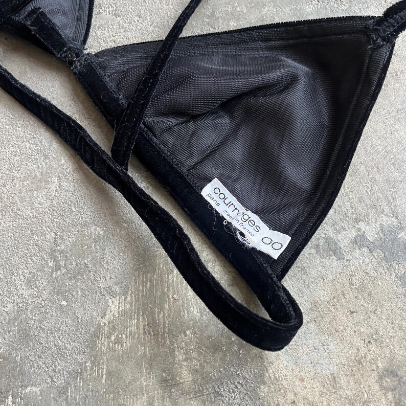 May include: Black velvet triangle bra with thin straps. The bra features a soft, textured fabric and a label that reads "courreges paris made in france". The bra is designed with a classic triangle shape.