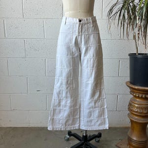 May include: White wide-leg pants with a grid-like pattern. The pants are displayed on a mannequin, showcasing the design and fit. The fabric appears to be a sturdy cotton or denim, with visible stitching defining the grid.