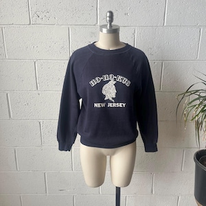 May include: Navy blue sweatshirt with the text "HO-HO-KUS" above an illustration of a Native American profile and the words "NEW JERSEY" below. The sweatshirt is displayed on a mannequin.