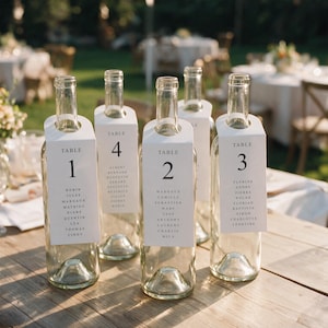 Peut inclure: Cinq bouteilles de vin en verre transparent posées sur une surface en bois, chacune dotée d'une étiquette de col en papier blanc imprimée avec un numéro de table et une liste de noms. Les étiquettes affichent Table 1, 4, 2 et 3 avec des noms.