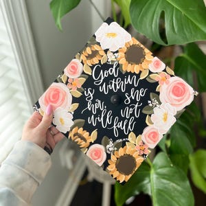 Könnte beinhalten: Eine schwarze Abschluss-Kappe, verziert mit Sonnenblumen, Rosen und anderen Blumen. Auf der Kappe steht der Text "Gott ist in ihr, sie wird nicht fallen" und "Psalm 46:5".