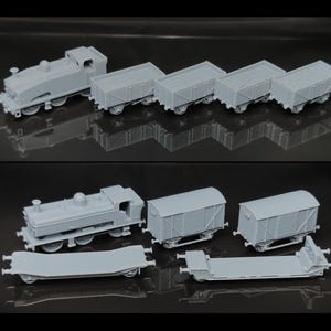 Puede incluir: Un conjunto de modelos de trenes grises, que incluye una locomotora, varios vagones de caja y vagones planos. Los vagones en miniatura están detallados con ruedas y elementos estructurales.