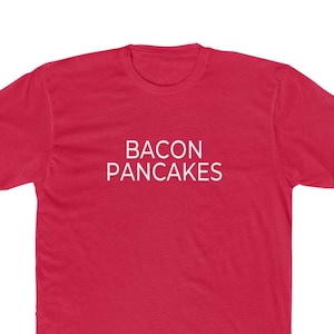 May include: A red t-shirt with the words "BACON PANCAKES" printed in white, centered on the front. The shirt has short sleeves and a crew neck.