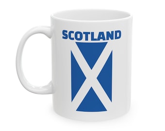 May include: White ceramic mug featuring the word "SCOTLAND" in blue block letters above a blue St. Andrew's cross design. The mug has a curved handle and a glossy finish, perfect for hot beverages.