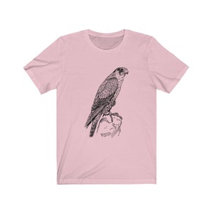 May include: A pink t-shirt featuring a black and white line drawing of a falcon perched on a rock.