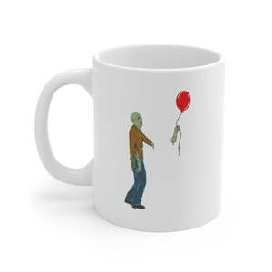 May include: White ceramic coffee mug with a cartoon illustration of a zombie holding a red balloon. The zombie is wearing a brown shirt and blue jeans.