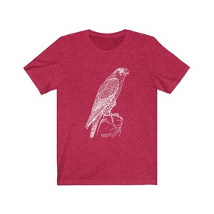 May include: A red heather t-shirt featuring a white outline drawing of a falcon perched on a rock.
