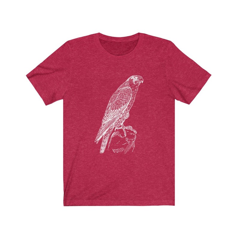 May include: A red heather t-shirt featuring a white outline drawing of a falcon perched on a rock.