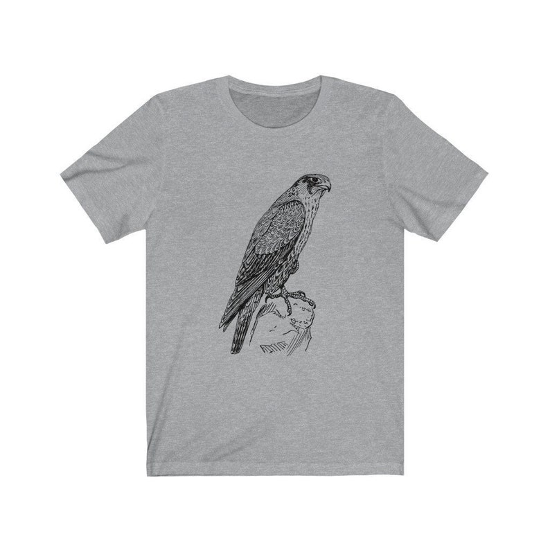 May include: A grey t-shirt featuring a black and white illustration of a falcon perched on a rock.