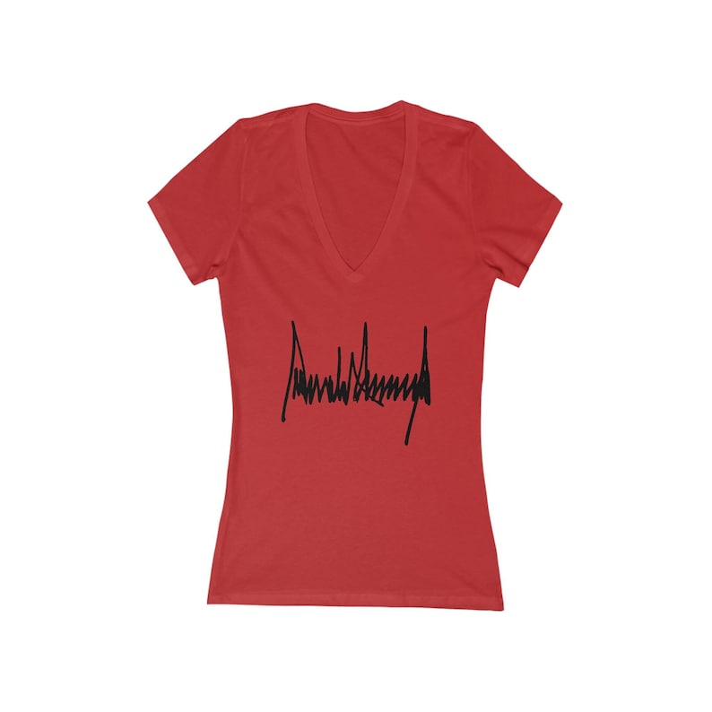 May include: Red V-neck t-shirt with a black signature that says "Donald J. Trump" on the front.