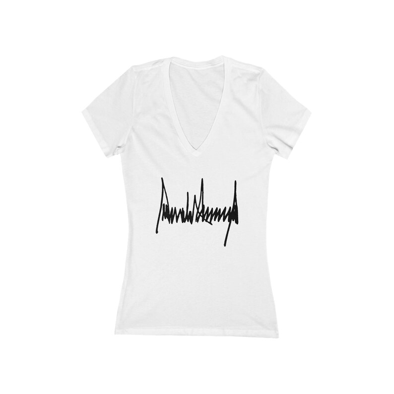 May include: White V-neck t-shirt with a black signature that reads "Donald J. Trump" printed on the front.