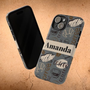 May include: A smartphone case with a coffee-themed design. The case features a gray background with coffee-related illustrations and the name "Amanda" in a white banner. The design includes coffee cups, croissants, and coffee beans.