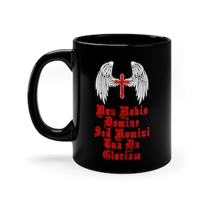 May include: Black ceramic mug with a white cross and wings design. The text "Non Nobis Domine Sed Nomini Tua Da Gloriam" is printed in red.