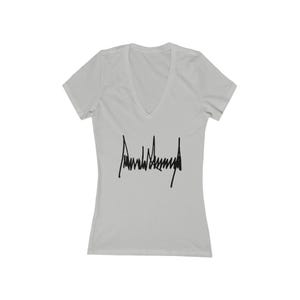May include: White V-neck t-shirt with a black signature that reads "Donald J. Trump" printed on the front.