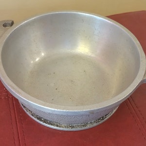 May include: A silver aluminum pot with two handles. The pot has a textured bottom and a smooth interior.
