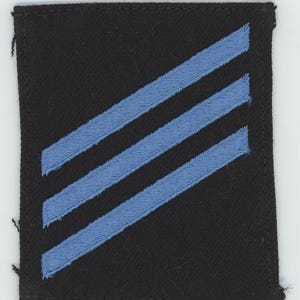 Op de afbeelding: Een zwarte stoffen patch met drie diagonale blauwe strepen.