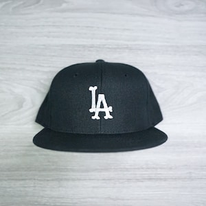 Peut inclure: Une casquette de baseball noire avec un logo "LA" blanc brodé sur le devant.