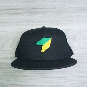 May include: Black baseball cap with a green and yellow geometric logo on the front.