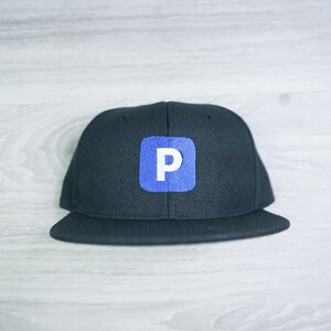 May include: Black and blue baseball cap with a white letter "P" in a square on the front.