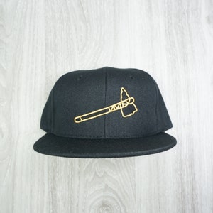 Puede incluir: Gorra de béisbol negra con un diseño de hacha de guerra bordado en oro.