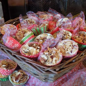 May include: A wicker basket filled with small, white, and brown cupcakes topped with shredded coconut. The cupcakes are decorated with red and green paper liners and wrapped in sheer white fabric.