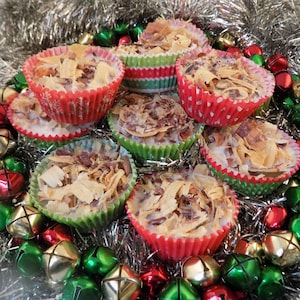 May include: A close-up of eight small, round, white chocolate peppermint bark candies topped with shredded coconut and pecans. The candies are in red and green paper cupcake liners and are arranged in a circle on a silver garland with red, green, and gold jingle bells.