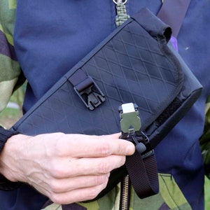 May include: A black crossbody bag with a diamond-patterned fabric and a silver buckle. The bag has a black adjustable strap with a silver clip.