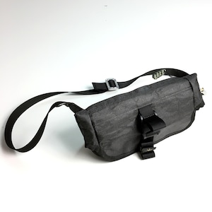 May include: A black crossbody bag with a silver buckle and a black strap. The bag has a flap with a buckle closure and a small pocket on the front.