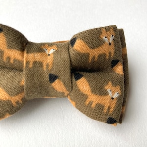 May include: A brown bow tie with a repeating pattern of orange foxes on a green background.
