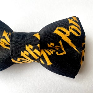 Könnte beinhalten: Ein schwarzer Fliege mit einem goldenen Muster aus den Worten "New York", die sich wiederholen.