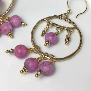 May include: Gold hoop earrings with a hammered finish and dangling pink and gold beads. The earrings are handmade and feature a unique design.