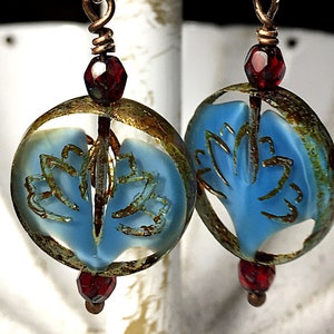May include: A pair of dangle earrings with blue and brown rectangular glass beads, a red glass bead, and a blue glass bead with a gold rim and a floral design.