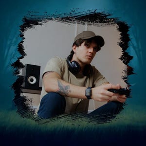 Puede incluir: Una persona joven con una gorra de béisbol marrón, una camiseta beige y pantalones vaqueros azules se sienta frente a un altavoz, sosteniendo un mando de videojuegos.