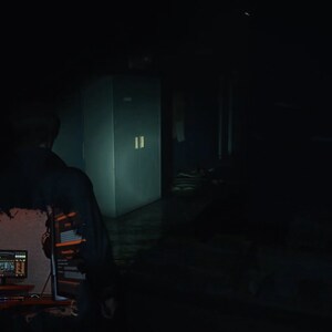 May include: A person wearing a hooded sweatshirt sits in front of a computer screen with a dark background. The screen displays computer code. The person is looking at the screen.