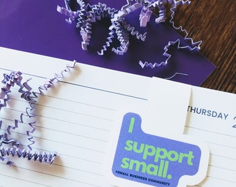 Op de afbeelding: Paarse en groene sticker met de tekst "I support small." en de hashtag "#smallbusinesscommunity".