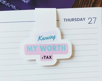 Op de afbeelding: Een roze en blauwe bladwijzer met de tekst "Knowing My Worth +Tax" op een witte achtergrond. De bladwijzer bevindt zich op een gelinieerde notitieboekpagina met de data "Donderdag 27" en "Vrijdag 28" die op de pagina zijn geschreven.