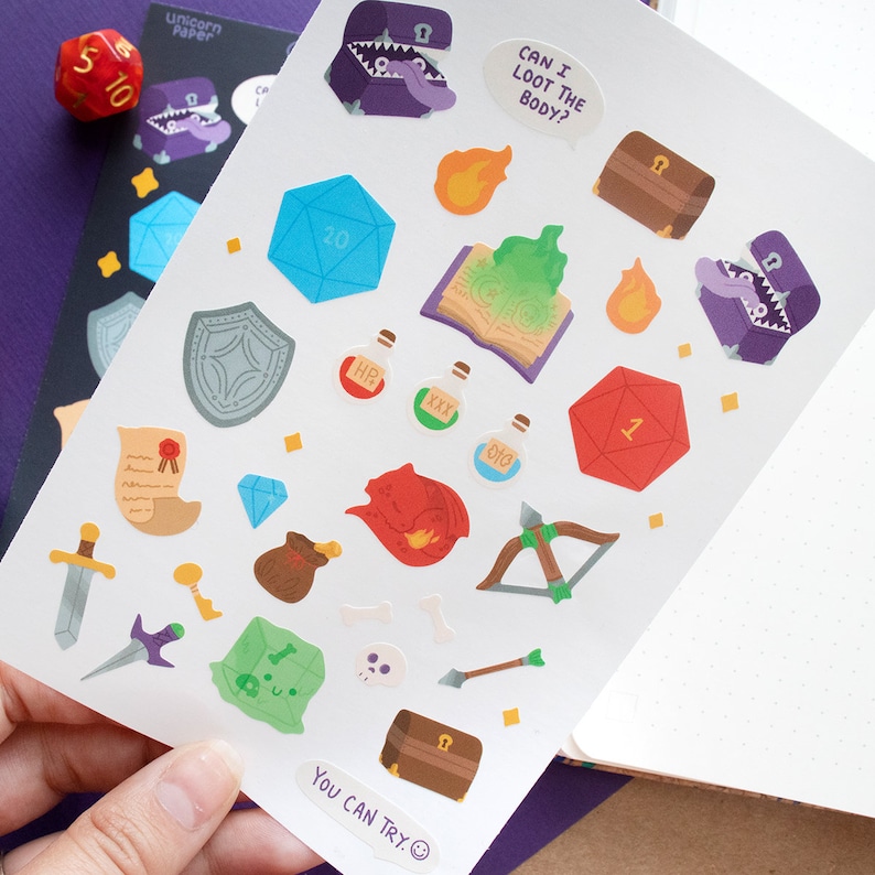 May include: A sheet of stickers featuring various fantasy and role-playing game themed illustrations, including dice, potions, a shield, a sword, a chest, a book, a skull, and a dragon. The text "CAN I LOOT THE BODY?" and "YOU CAN TRY." are also included on the sheet.