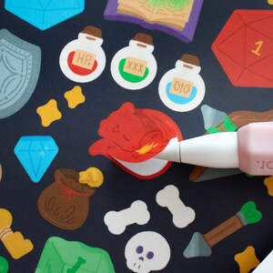 May include: A close-up of a red dragon sticker being applied to a black background with various other stickers, including a blue diamond, a brown bag, a green potion bottle with the text "XXX", a blue potion bottle with the text "OTC", a yellow bone, a green gem, and a white skull.