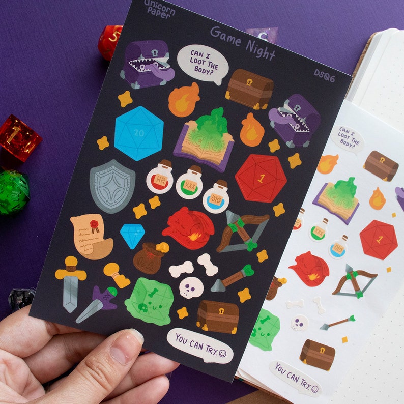 May include: A sheet of black and white stickers with a game night theme. The stickers feature various images related to role-playing games, including dice, treasure chests, potions, and a dragon. The text "Game Night" is printed at the top of the sheet. The text "Can I loot the body?" is printed on a speech bubble above a purple monster.