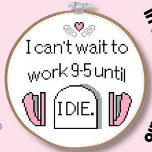 May include: A cross-stitch embroidery hoop with a white background and black text that reads "I can't wait to work 9-5 until I DIE." The text is surrounded by pink hearts and wings. The hoop is made of wood and has a natural finish.