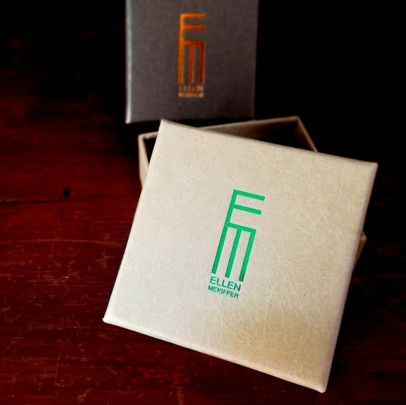 May include: A white box with a green logo that says "Ellen Mekiffer" and the letters "EM" in a stylized font.
