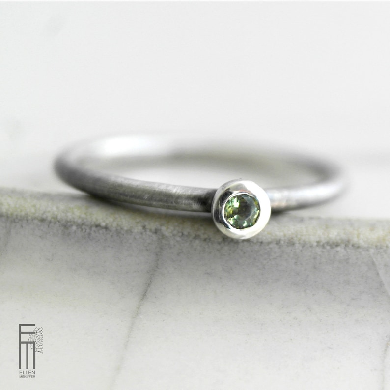 May include: A simple silver band ring with a small, round green gemstone set in a bezel setting.