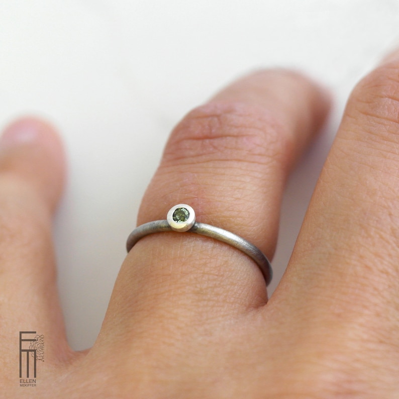 May include: A silver ring with a small, round, green gemstone set in the center.
