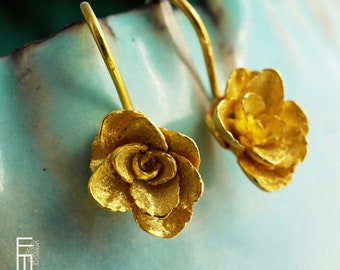 Può includere: Un paio di orecchini pendenti dorati a forma di rosa. Gli orecchini hanno una semplice chiusura a gancio.
