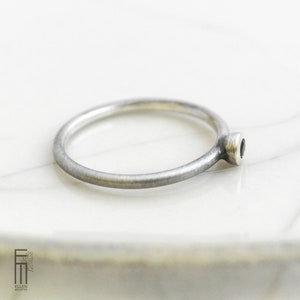 May include: A simple silver band ring with a small black gemstone set in a silver bezel.