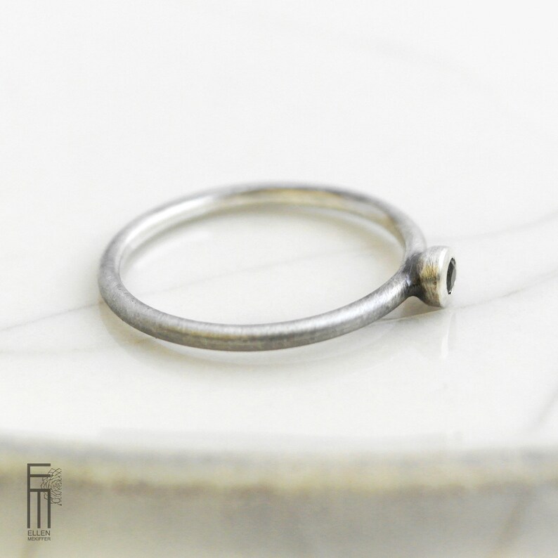 May include: A simple silver band ring with a small black gemstone set in a silver bezel.