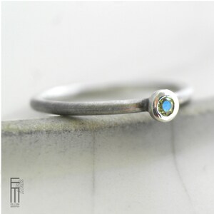 May include: A silver ring with a small, round, blue and green gemstone.